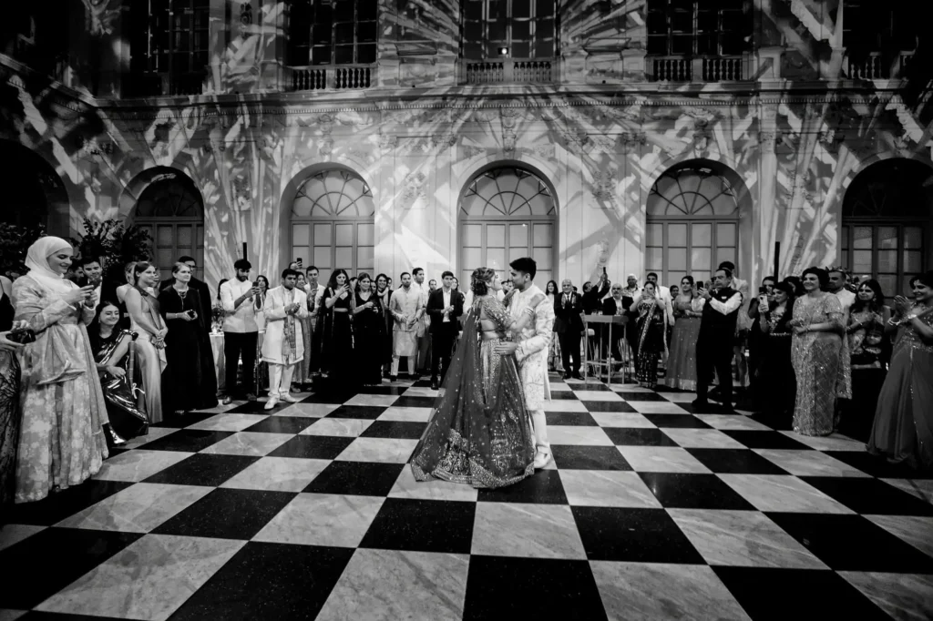 Elegant Indian wedding couple dancing on checkered floor in ornate Cartagena hall, surrounded by guests in traditional attire, capturing joyful cultural celebration — John Palacio