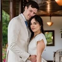 Joyful bride and groom embrace closely under a wooden porch in Pereira, with tropical greenery and warm lights creating a romantic wedding atmosphere — John Palacio
