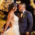 Bride in lace gown and groom in navy tuxedo share a tender moment at a glowing bar with golden lights and floral accents in Medellín, evoking joyful wedding romance — John Palacio